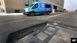 An electric van drives past a visible in-road wireless charging coil to be installed in a street in Detroit, Wednesday, Nov. 29, 2023. (AP Photo/Paul Sancya)