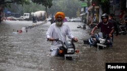 ভারতের নয়াদিল্লিতে প্রবল বৃষ্টির পর লোকজন তাদের মোটরবাইকে করে বন্যা প্লাবিত রাস্তা পার হচ্ছে। ৯ জুলাই, ২০২৩। 