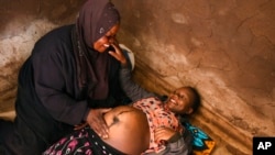 FILE - A traditional birth attendant attends to a pregnant woman at her home, in Simika Village, Chiradzulu, southern Malawi, May 23, 2021. 