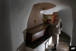A faithful holds a candle as she prays at a sarcophagus with holy relics in the underground labyrinth of the Monastery of the Caves, one of the holiest sites of Eastern Orthodox Christians, in Kyiv, March 24, 2023.