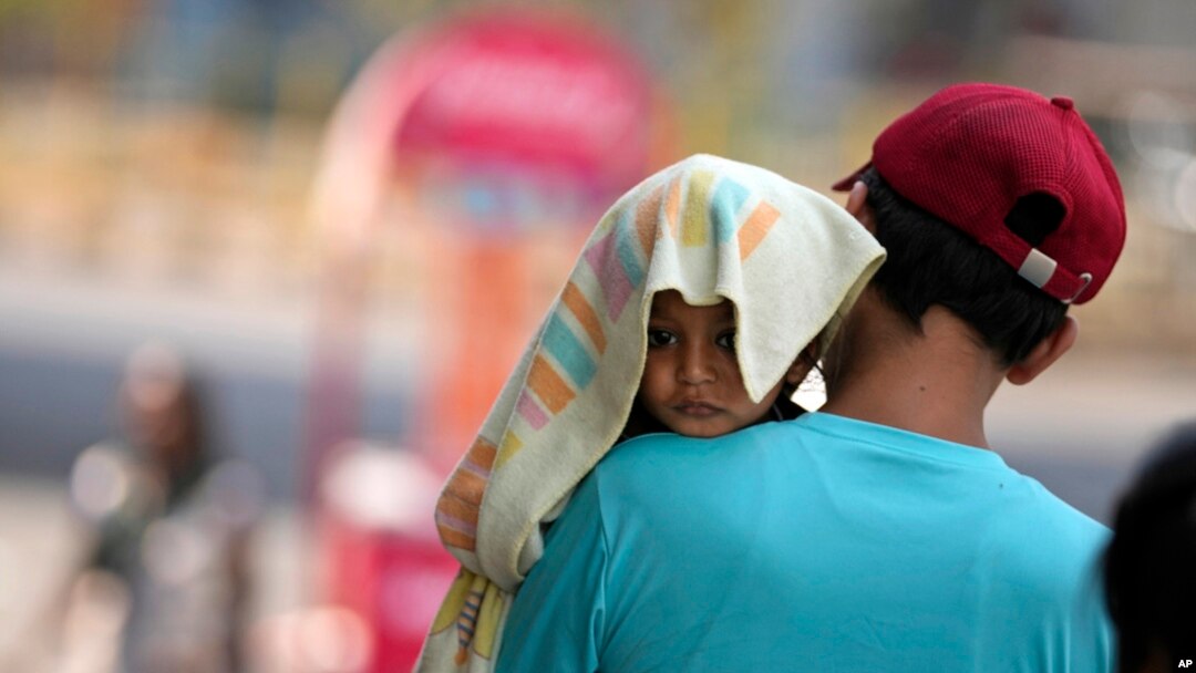 FILE- A man carries a child, head covered with a towel to protect from the heat, in Jammu, India, June 2, 2024.