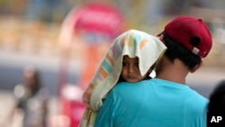 FILE- A man carries a child, head covered with a towel to protect from the heat, in Jammu, India, June 2, 2024.