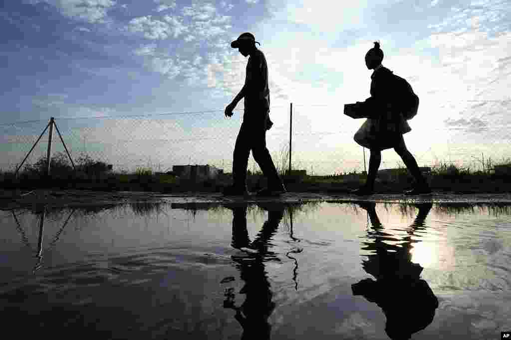 A man and woman walks over puddled water along a street from an overflowing reservoir in Hamanskraal, Pretoria, South Africa, Friday, May 26, 2023.&nbsp;