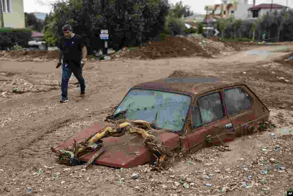 A man walks next to a damaged car after floods in the town of Agria near the city of Volos, Greece.