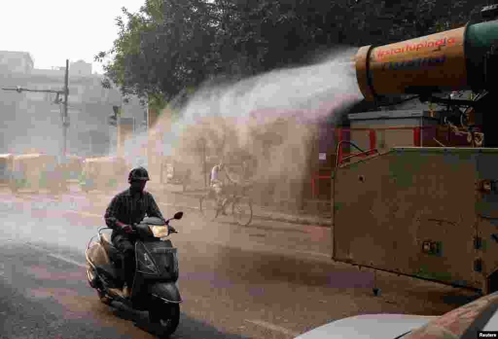 A scooter passes by an anti-smog gun being used to reduce pollution, on a smoggy morning in the old quarters of Delhi, India.
