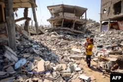 A woman stands holding a child surrounded by the rubble of buildings destroyed during Israeli bombardment in Khan Yunis on the southern Gaza Strip, June 23, 2024.