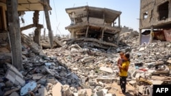A woman stands holding a child surrounded by the rubble of buildings destroyed during Israeli bombardment in Khan Yunis in the southern Gaza Strip on June 23, 2024. 