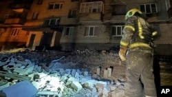 In this photo provided by the Ukrainian Emergency Service, a firefighter examines damage to an apartment building following a Russian drone attack in Dnipro, Ukraine, Feb. 23, 2024.