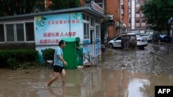 A man walks along a water laden street, after heavy rains in Mentougou district in Beijing on July 31, 2023.