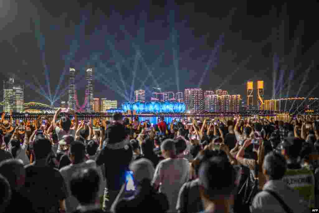 People gather at the promenade of Qiantang River to watch the light show of the Hangzhou Olympic Sports Centre Stadium (C), ahead of the 2022 Asian Games in Hangzhou in China&#39;s eastern Zhejiang province. (Photo by Philip FONG / AFP)