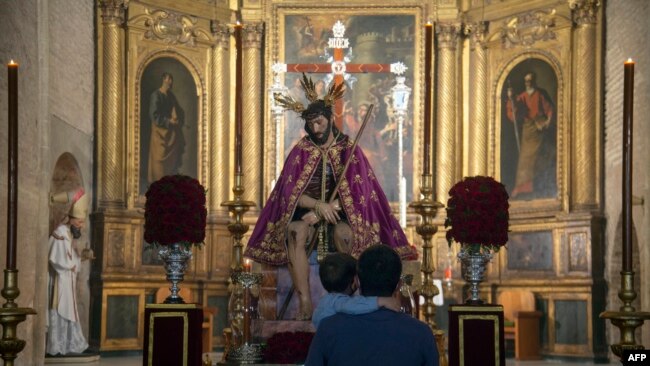 FILE - A father and his son look at a figure of Jesus Christ at San Esteban church, in Seville, Spain, on March 30, 2021.