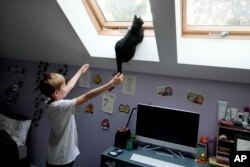 Julian Kozak, 9, plays with his cat at home in Warsaw, Poland, April 5, 2024. Starting this month, he has more time to play because Poland's government has ordered limits on the amount of homework teachers can assign students in lower grades.