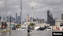 Seseorang berjalan di genangan banjir akibat hujan lebat, dengan latar belakang menara Burj Khalifa di Dubai, Uni Emirat Arab, 17 April 2024. (REUTERS/Amr Alfiky)