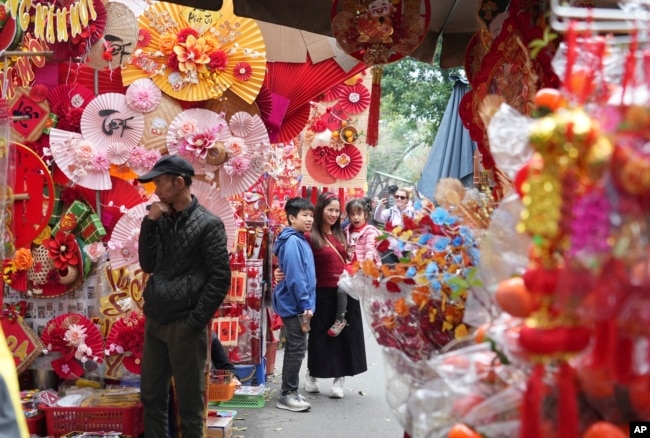 People pose for photos in a traditional Lunar New Year market in Hanoi, Vietnam Thursday, Feb. 8, 2024. Vietnam is preparing to welcome the Lunar New Year of the Dragon, the most popular festive event of the year. (AP Photo/Huy Han)