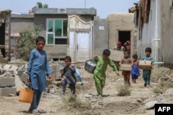 Anak-anak Afghanistan membawa barang-barang mereka setelah banjir bandang di daerah Khair Abad di Provinsi Ghazni pada 23 Juli 2023. (Foto: AFP)