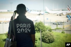 Seorang sukarelawan Olimpiade Paris mengamati pesawat di landasan bandara Charles de Gaulle, 19 Juli 2024 di Roissy, utara Paris. (Foto: AP)