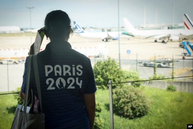 Seorang relawan Olimpiade Paris mengawasi pesawat di landasan pacu bandara Charles de Gaulle, 19 Juli 2024, di Roissy, sebelah utara Paris. Gangguan teknis pada sistem komputer global maskapai penerbangan menyebabkan penundaan penerbangan di dua bandara utama di Paris.