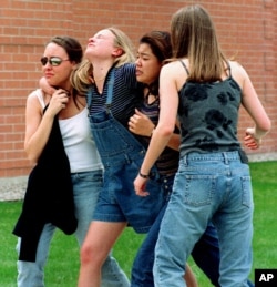 FILE - Young women visit a library near Columbine High School where students and faculty members attend after a shooting by two gunmen at the school in Littleton, a southwest suburb of Denver, Colorado, April 20, 1999 People were evacuated.