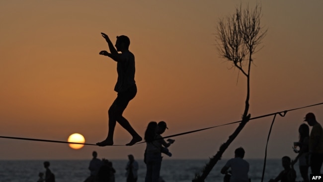 A man is silhouetted against the setting sun as he balances on a wire at a beach in the Israeli coastal city of Tel Aviv, Israel, on April 19, 2024.