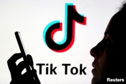 Seseorang memegang smartphone dengan latar belakang logo TikTok dalam sebuah ilustrasi pada 7 November 2019. (Foto: REUTERS/Dado Ruvic)