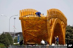 FILE - Workers install wires on a "Golden Bridge of Silk Road" structure on a platform outside the National Convention Center, the venue that held the Belt and Road Forum for International Cooperation, in Beijing, April 18, 2017.