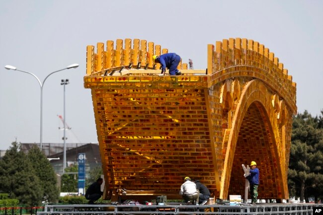 FILE - Workers install wires on a "Golden Bridge of Silk Road" structure on a platform outside the National Convention Center, the venue that held the Belt and Road Forum for International Cooperation, in Beijing, April 18, 2017.