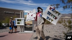 A demonstrator protests visitors to Death Valley National Park, July 16, 2023, in California. Death Valley's brutal temperatures and heat index come amid a blistering stretch of hot weather that has put roughly one-third of Americans under some type of heat advisory, watch or warning. The thermometer, at left, is not official but is a popular photo spot.