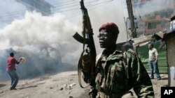 FILE - In this Wednesday, January 2, 2008 file photo, an armed police officer walks past burning buildings during post-election rioting in the Mathare slum of Nairobi, Kenya.