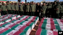 FILE - Revolutionary Guard members stand over the flag-draped coffins of victims a bomb explosion during their funeral ceremony in the city of Kerman, Iran, Jan. 5, 2024. The Iranian government linked the attack to ethnic-Tajik fighters of the Islamic State Khorasan Province.