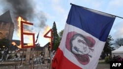 A protester hold a French flag beside a wooden "64" set afire outside the Prefecture of Sarthe in a demonstration after France's Constitutional Council approved the key elements of a pension reform, in Le Mans, France, on April 14, 2023. 