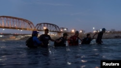FILE - Migrants link arms with each other as they wade into the Rio Grande River with intentions to cross into Eagle Pass, Texas, U.S., in Piedras Negras, Coahuila, Mexico, Feb. 24, 2024. 