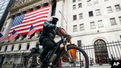 FILE - Seorang pekerja pengiriman barang mengendarai sepeda listriknya melewati New York Stock Exchange di New York, 16 Maret 2020. (AP/John Minchillo, File)