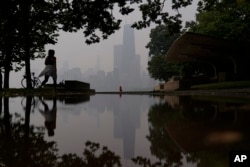 A person walks along the shore of Lake Michigan as the downtown skyline is blanketed in haze from Canadian wildfires, June 27, 2023, in Chicago.