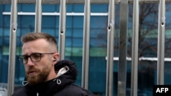 A journalist reports near the fence with scared with bullet holes in front of Top Channel television, in Tirana, Albania, on March 27, 2023.