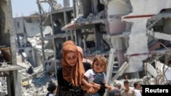 A Palestinian woman holds her daughter as she walks past the rubble of houses destroyed during the Israeli military offensive, amid Israel-Hamas conflict, in Khan Younis in the southern Gaza Strip, July 10, 2024.