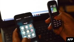Foto ilustrasi yang menunjukkan seseorang menggunakan ponsel pintar dan telepon genggam bersamaan. (Foto: AFP/Issouf Sanogo)