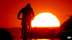A man rides a bike on a small road on the outskirts of Frankfurt, Germany, as the sun rises on July 7, 2023.