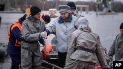 Emergency workers help a woman get off a boat during evacuations of local residents in a flooded street after a part of a dam burst, in Orsk, Russia, April 8, 2024.