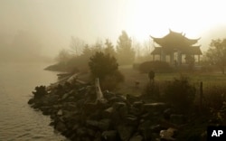 FILE - A woman walks her dog through morning fog near the Fuzhou Ting Pavilion at the Chinese Reconciliation Park in Tacoma, Washington, on Dec. 7, 2017. The pavilion was donated by officials in Fuzhou, China, one of Tacoma's sister cities.