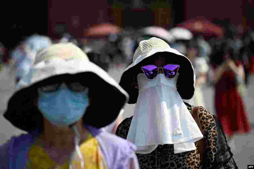 Women shelter under hats and masks as they walk out of the Forbidden City during hot weather conditions in Beijing.