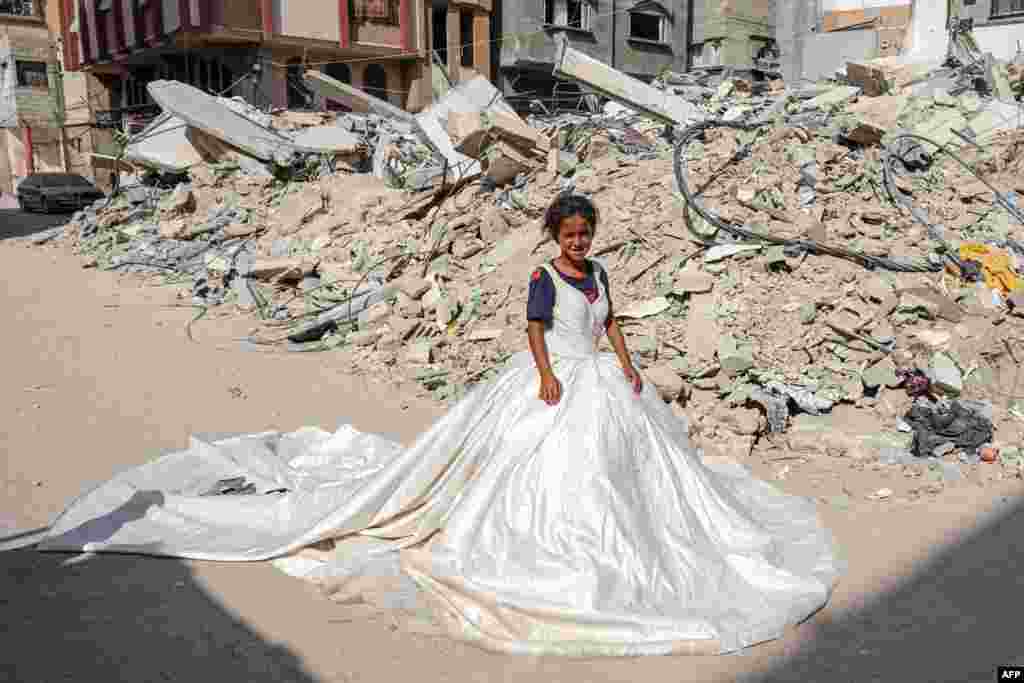 A Palestinian girl poses with a wedding dress found amid the rubble of buildings destroyed during Israeli bombardment, in Khan Yunis in the southern Gaza Strip.