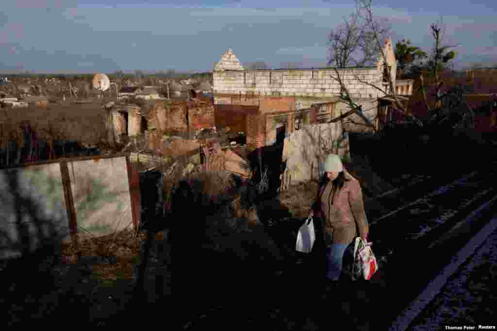 Una mujer local carga comestibles cerca de las casas dañadas durante los combates.