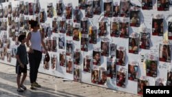 A woman and child walk by a wall with pictures of people held in Gaza after they were kidnapped from Israel by Hamas gunmen on Oct. 7, as families and supporters of hostages hold a demonstration calling for their release in Tel Aviv, Nov. 3, 2023.