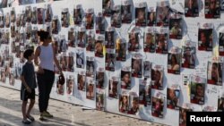 ফাইল ছবি—হামাসের যোদ্ধাদের হাতে জিম্মি হয়েছেন এমন কিছু মানুষের ছবির সামনে দিয়ে হেঁটে যাচ্ছেন এক নারী ও এক শিশু।