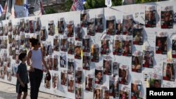 FILE - A woman and child walk by a wall with pictures of people held in Gaza after they were kidnapped from Israel by Hamas gunmen. A group of family members of hostages is asking prosecutors at the International Criminal Court to bring charges against Hamas leaders.