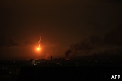 A picture taken from Rafah shows a flare lighting the sky as smoke billows following Israeli bombardment of Khan Yunis in the southern Gaza Strip on Dec. 9, 2023.