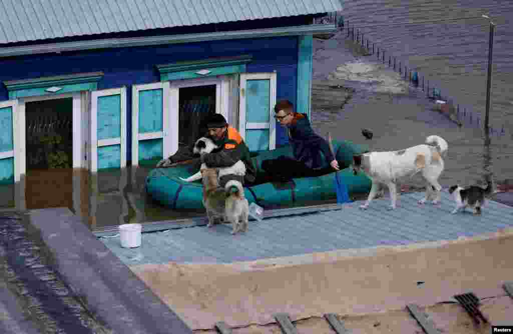 Local resident Alexander Timofeyevich, left, sails with a neighbor on an inflatable boat through the flooded yard of his house to feed the dogs stranded on the roof, in Orenburg, Russia.