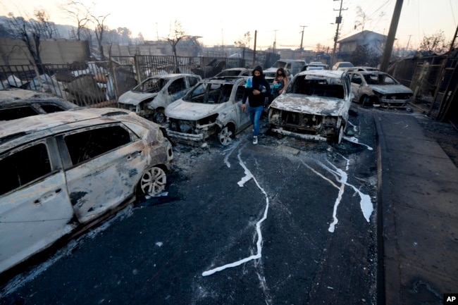Locals walk among burnt cars after a forest fire reached the neighborhood of Villa Independencia in Vina del Mar, Chile, Feb. 3, 2024.