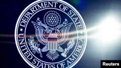 U.S. Secretary of State Antony Blinken is seen reflected at right next to a State Department logo at right as he speaks during a staff event at the State Department in Washington, March 31, 2023.