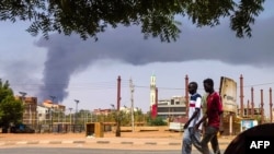 Men walk down a street in Khartoum on June 8, 2023, as smoke rises from behind buildings amid continuing fighting between the army and paramilitary forces. 
